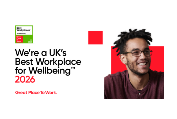 A smiling man looks out, against a red graphic backdrop. The text reads: "We're a UK's Best Workplace for Wellbeing 2026. Great place to Work". The graphic also features a "Best workplace for wellbeing 2026" badge.